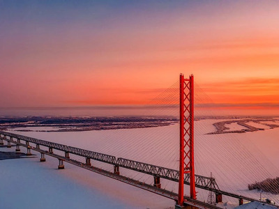 Югорский мост
Вантовый исполин над Обью. Это не просто мост, это символ триумфа человеческой инженерной мысли над суровой сибирской природой и географией. Перекинувшись через широкую и полноводную Обь, этот гигант на момент своего открытия в 2000 году установил мировой рекорд Гиннесса как мост с самым длинным однопилонным пролетом — целых 408 метров! Общая длина сооружения — впечатляющие 2110 метров. Его единственный пилон взмывает в небо на 150 метров, а натянутые от него стальные канаты создают ощущение гигантской арфы. Особенно завораживающе мост выглядит в ночной подсветке, когда он превращается в сияющий шлейф огней над темными водами Оби.